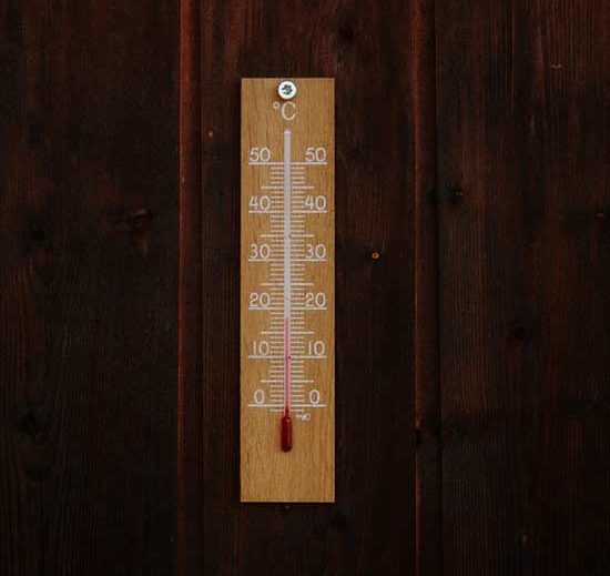 A wooden thermometer laid on top of boards of wood flooring.