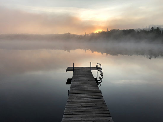 Dock of wooden planks in a foggy weather, before sunrise as discuss wood’s moisture content during acclimation process.