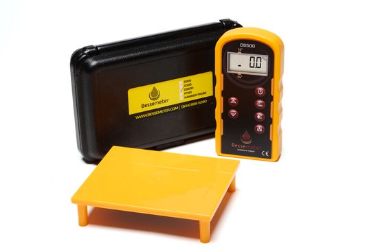 A yellow Bessemeter wood moisture meter with a black case and a calibration verification reference