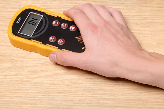 A hand holding a Bessemeter S300 on a flat surface of wood