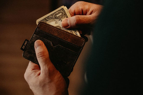 A hand pulling cash out of a leather wallet to pay for damage caused by failing to use a moisture meter