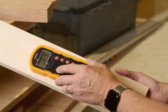Someone uses a handheld pinless wood moisture meter from Bessemeters to measure a piece of wood.