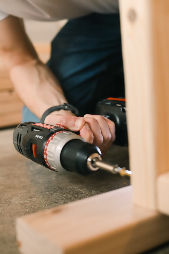 A woodworker using a cordless power drill to screw two pieces of wood together