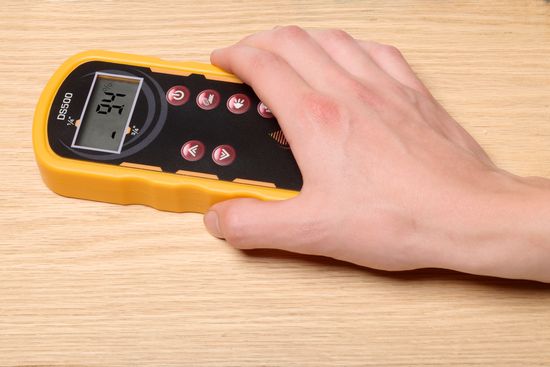 A hand holding a yellow pinless moisture meter on a piece of wood