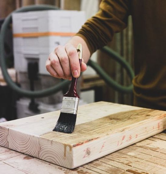 A woodworker applying varnish to a piece of wood