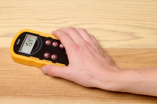 A hand holding a pinless moisture meter on a board of wood