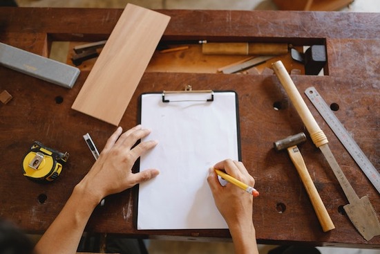 A hand sketching out project plans on a desk covered in woodworking tools