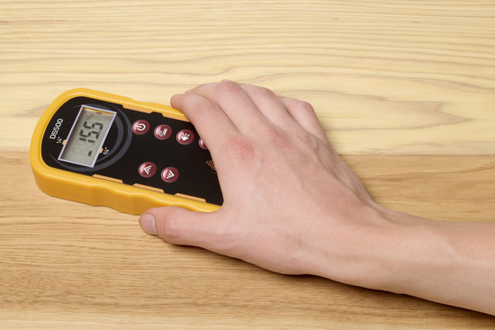 A hand holding a moisture meter and taking a reading of a floating floor