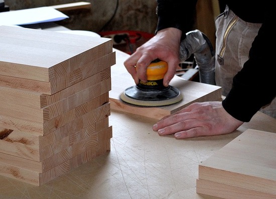 A professional woodworker using an orbital sander on a piece of wood that was kiln dried