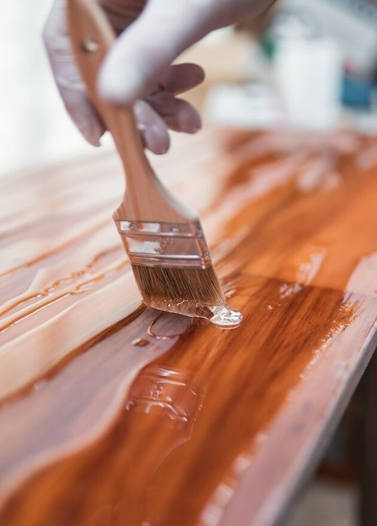 A hand holding a paintbrush and applying finish on a piece of wood