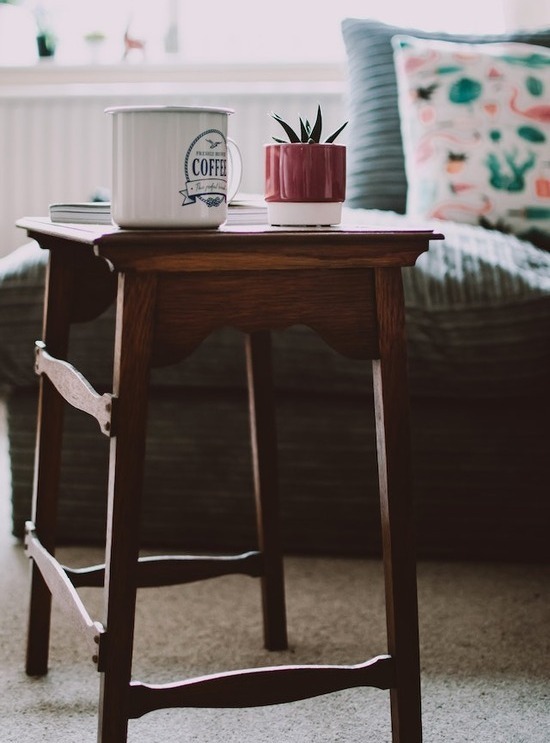 A hardwood side table with a small plant and mug of coffee on it
