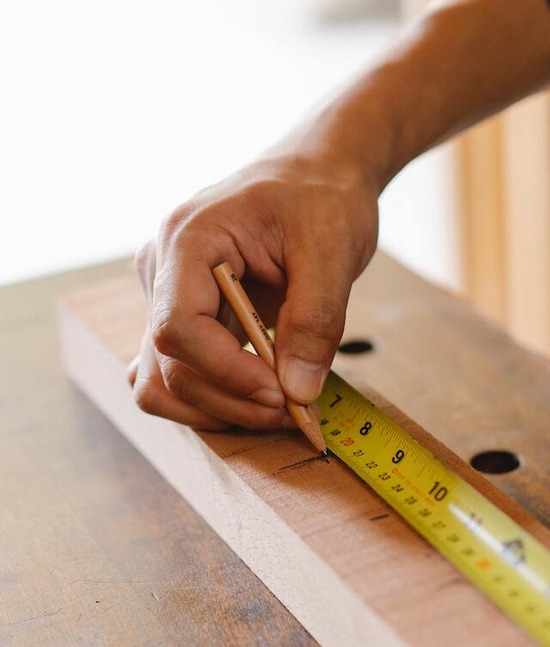 A hand holding a tape measure and marking spots on a piece of wood