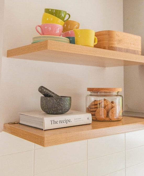 Wood Floating Shelves Two floating shelves with mugs, a recipe book, and a jar of cookies