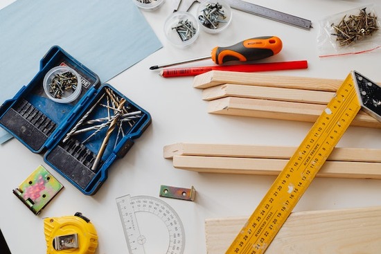 Screws, a screwdriver, tape measure, ruler, wood pieces, and pencil scattered on a work table