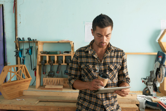 A carpenter holding an iPad and looking at woodworking plans