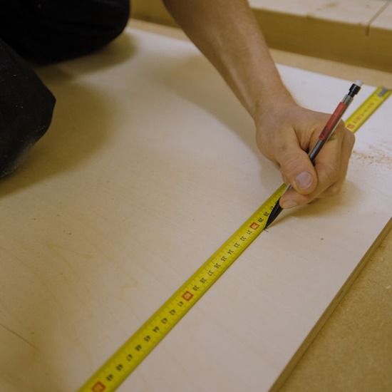 A hand marking measurements on a board of wood