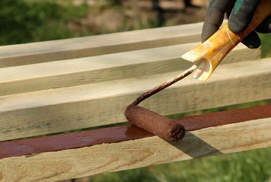Four boards being painted a rich chocolatey brown with a paint roller