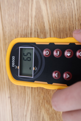 A hand holding a moisture meter on a piece of wood