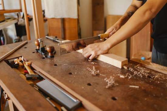 A woodworker cutting a piece of wood with a handsaw