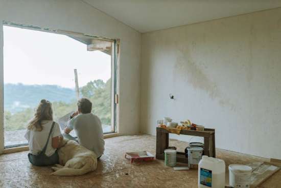 Two people and a dog sitting in a room with the old flooring removed