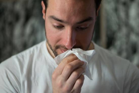 A man with allergies wiping his nose with a tissue.