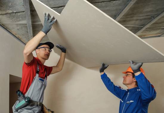 Two installers lifting a sheet of drywall into position.