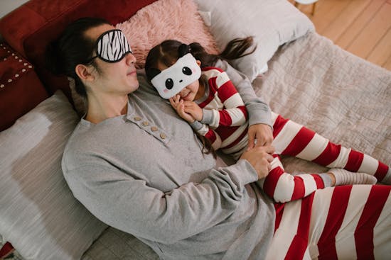 A father and daughter lying in bed wearing sleep masks