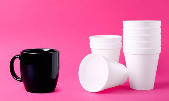A black mug standing next to stacks of white Styrofoam cups